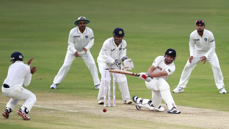A batter plays a sweep shot with the wicketkeeper and close fielders watching.