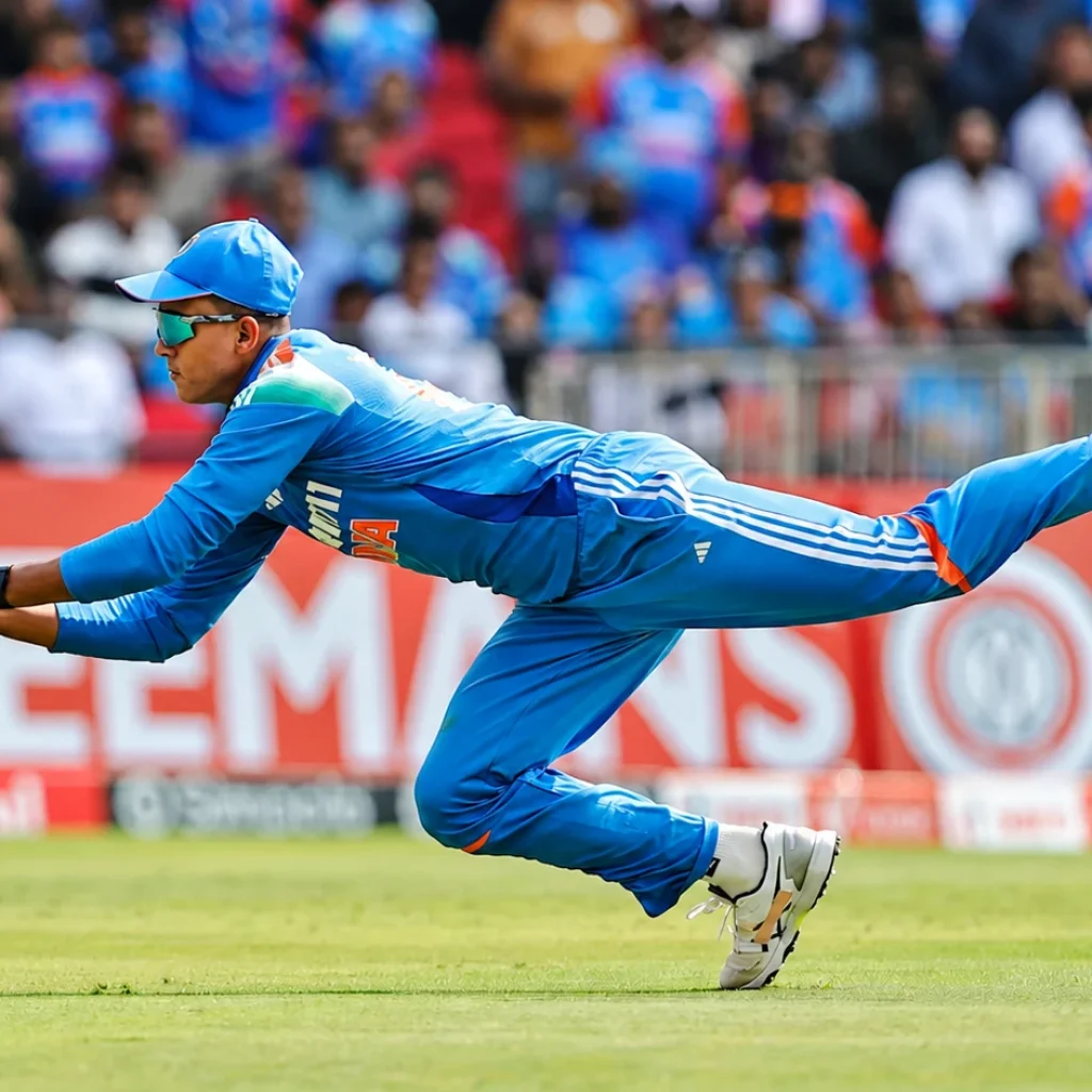 Indian cricketer in blue diving forward with both hands extended to catch the ball.