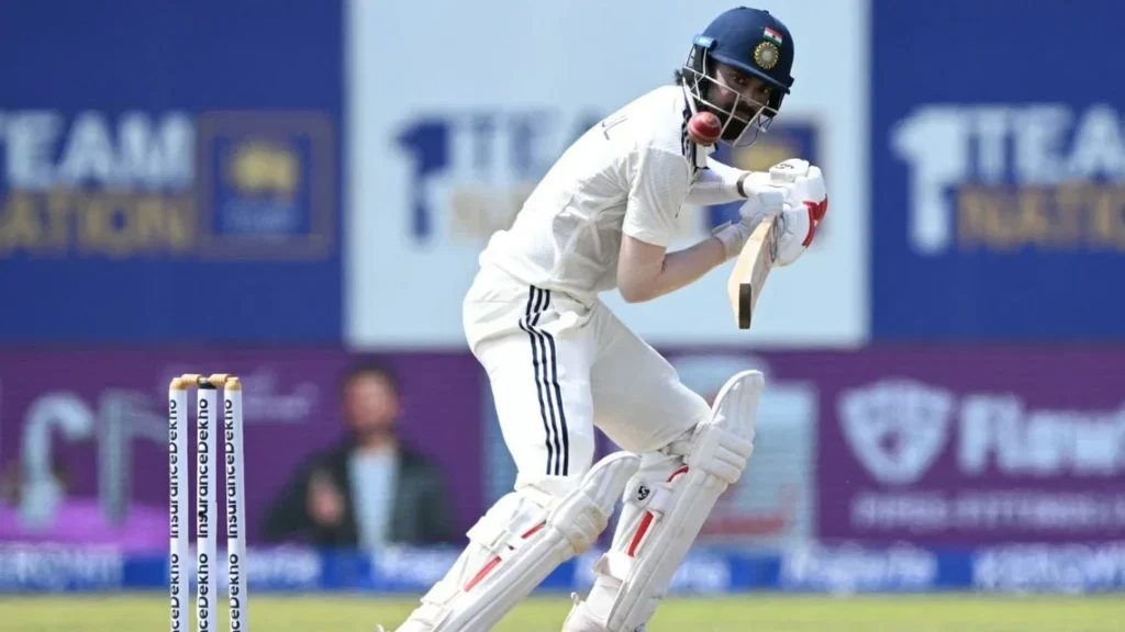 A batter in white cricket clothing and an India helmet plays a red ball.
