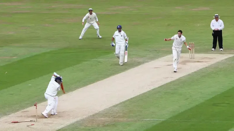 A fast bowler follows through as a batter plays a shot in a red-ball match.